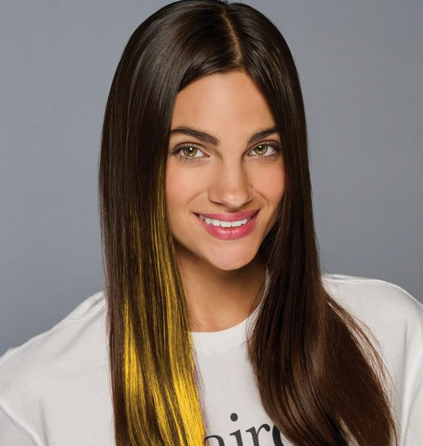 Woman with long brown hair featuring a yellow streak, wearing a white shirt.