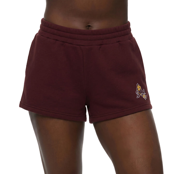 A close-up of a person wearing burgundy sweat shorts with a small embroidered mascot logo on the lower left leg, shown against a plain white background.