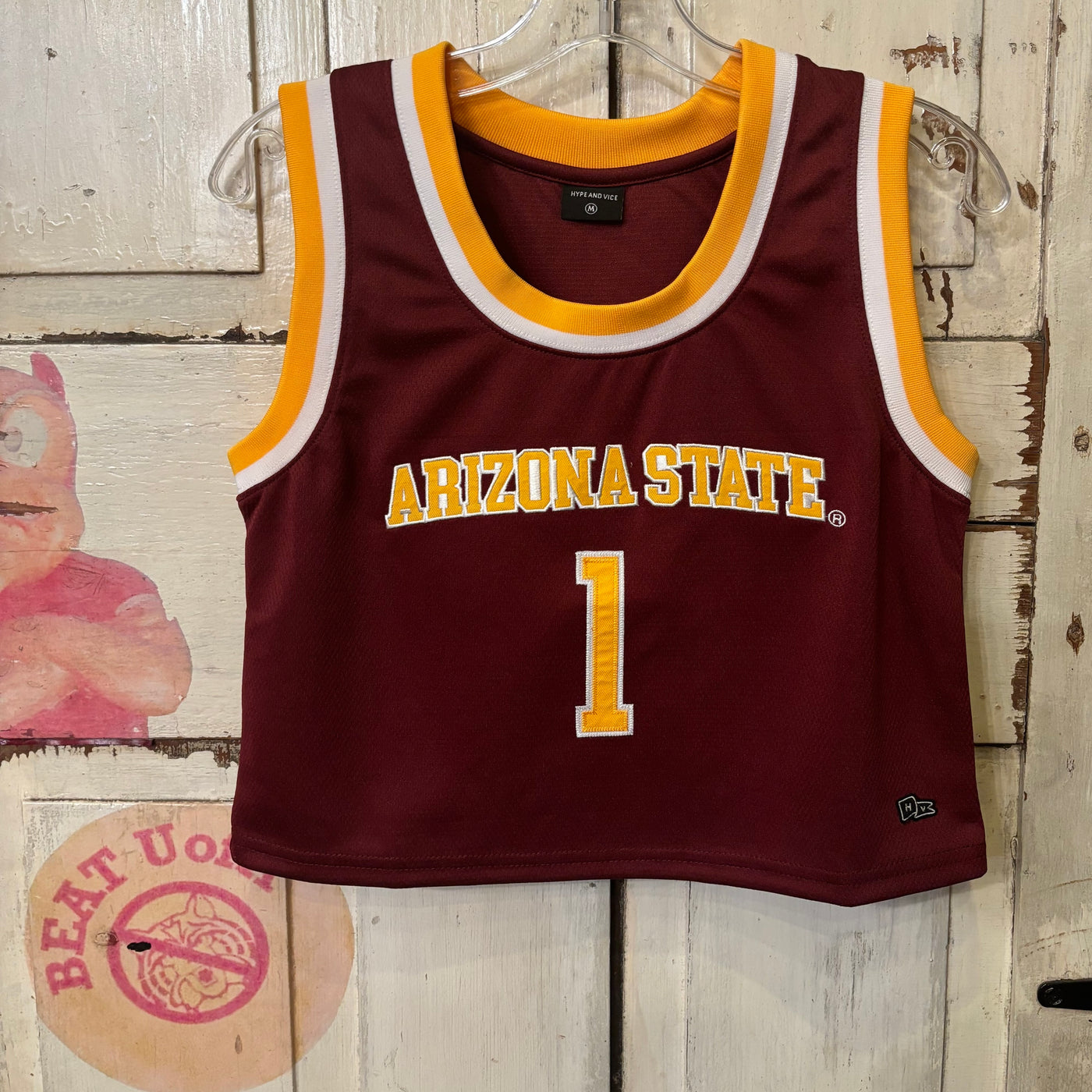 ASU maroon cropped basketball jersey. The ends of the sleeves and collar are outlined by a solid white line and a solid gold line. Across the chest reads 