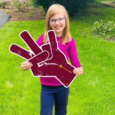 Girl holding an ASU lawn sign in grass of maroon hand with a gold pitchfork on the wrist making the 'pitchfork' sign