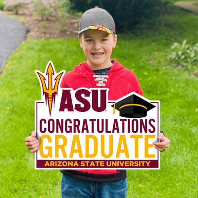 Boy hold a sign in a yard that is saying 'ASU, Congratulations, Graduate, Arizona State University" with a pitchfork and a graduation cap at the top