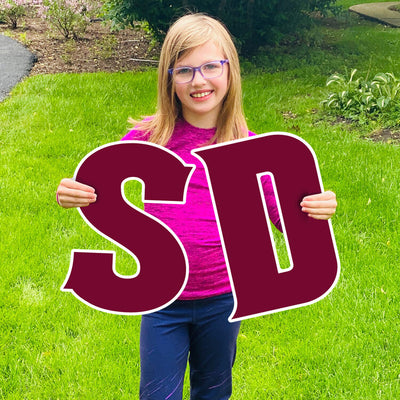 Girl holding 'S' and 'D' lawn sign letters in maroon